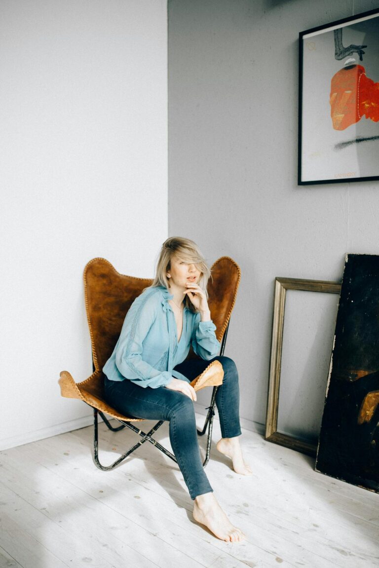 A stylish woman sitting in a modern, minimalist room with art on the wall.
