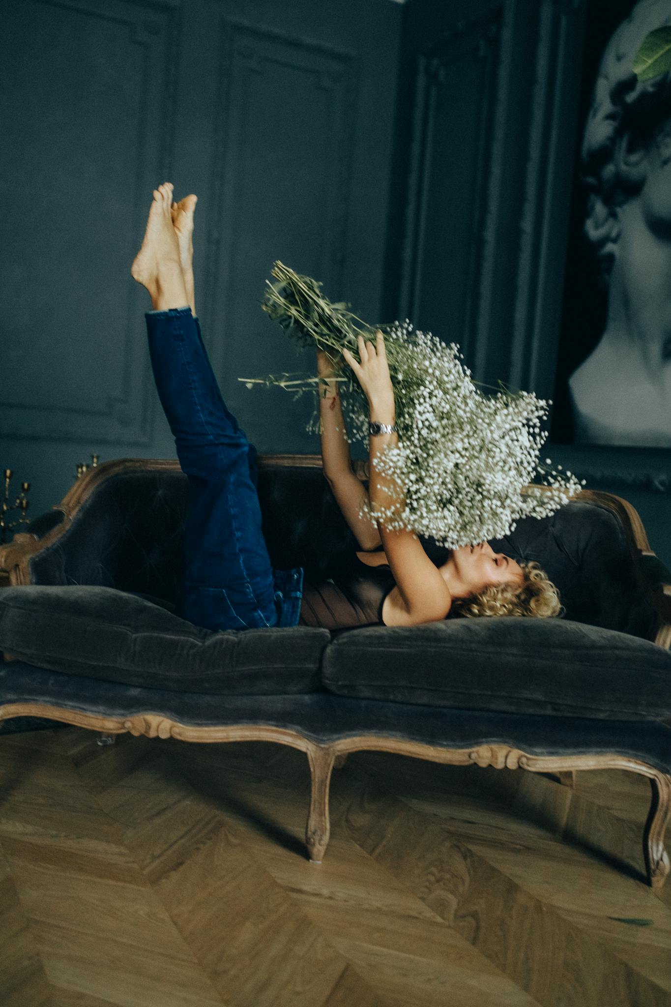 A woman lounging on a vintage sofa holding white flowers, creating a relaxing home vibe.